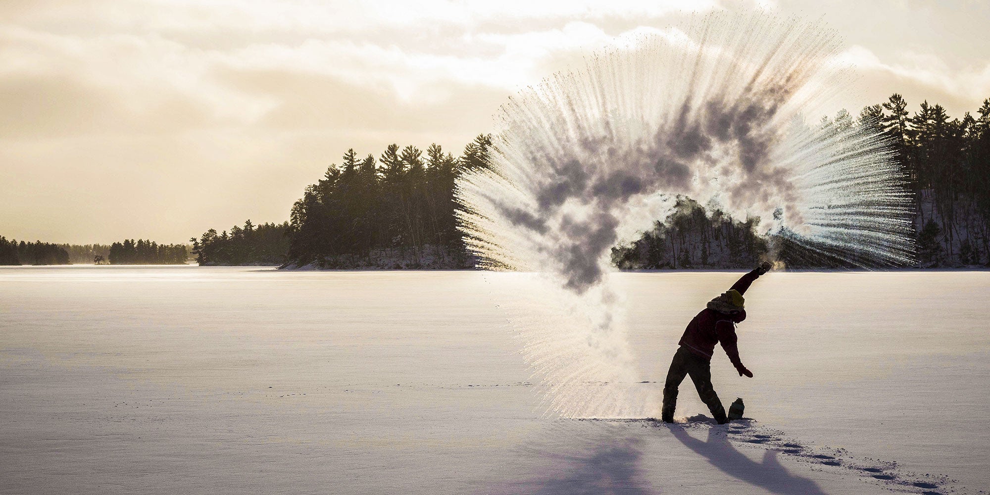 Woman in front of sunset throwing hot water into sky on cold day for circular evaporation effect.